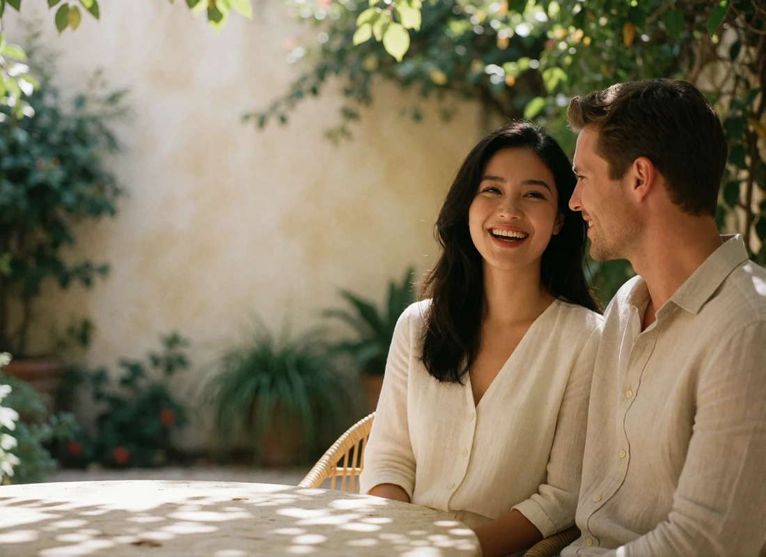 Couple sitting together at a shaded courtyard table in light linen clothing, laughing gently