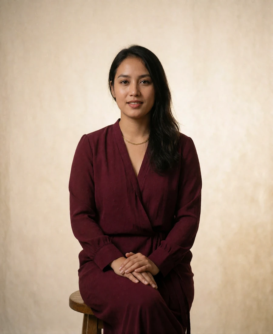 Nepali woman in a deep burgundy blouse seated on a wooden stool against an ivory studio backdrop