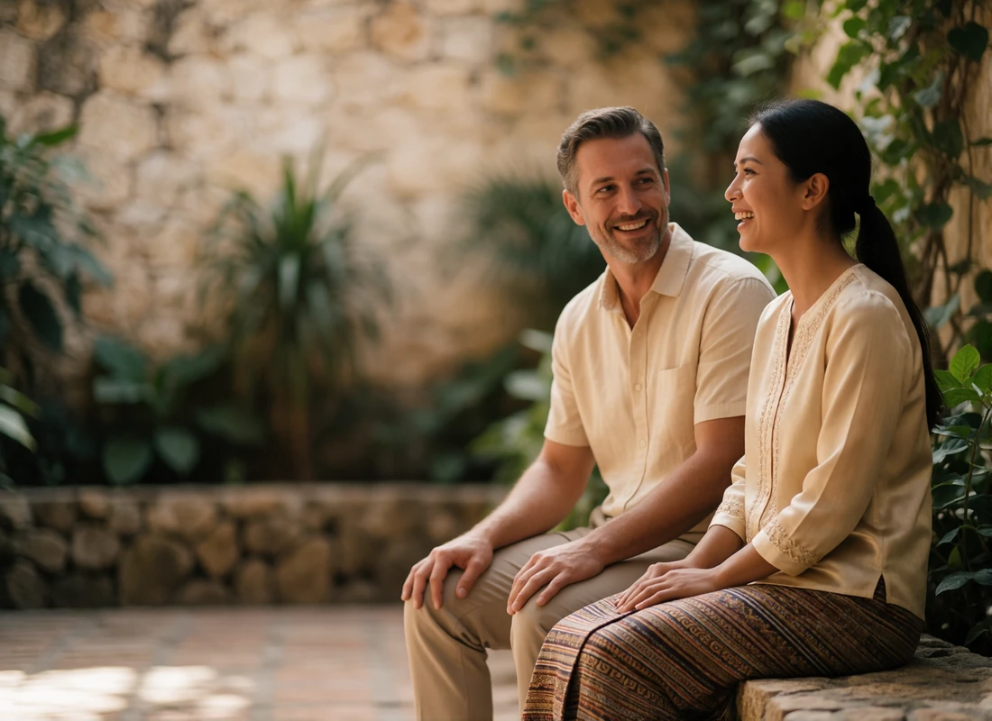 Laotian woman and Western man sitting together on a stone bench in a shaded courtyard in relaxed conversation